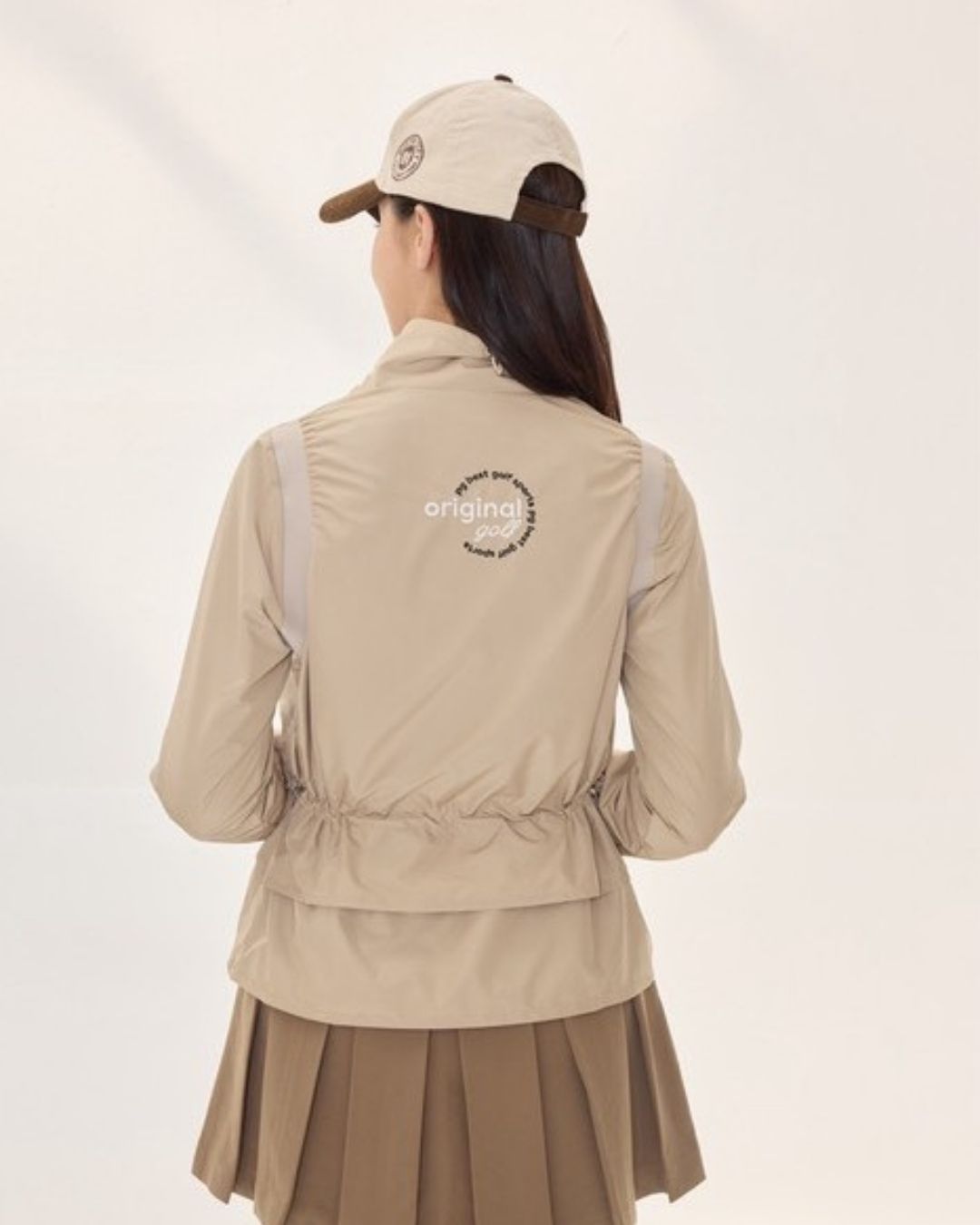 Chamuleのベージュのウエストドロストジャケット。背面にロゴプリントがあり、スタンドカラーとレイヤード風の裾が特徴的なゴルフウェア。