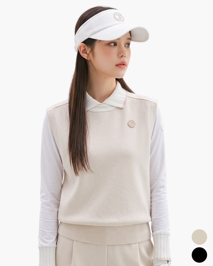 Chamuleのベージュのシンプルゴルフベストを着用した女性。白の長袖シャツとサンバイザーを合わせた上品なレイヤードスタイル。