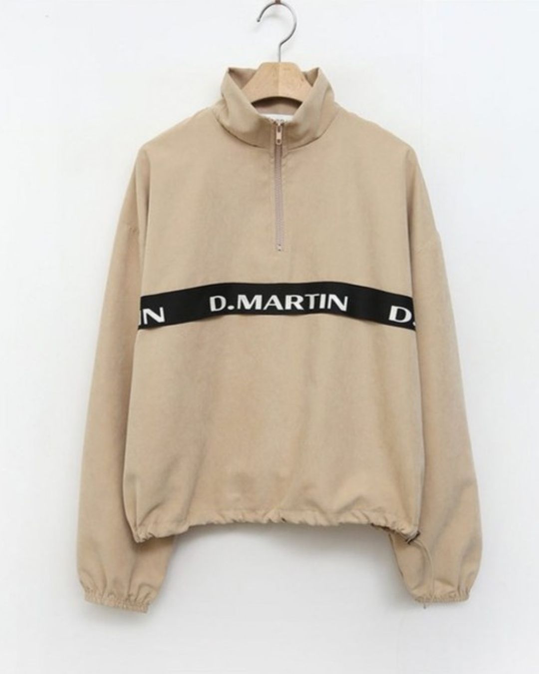 Chamuleのベージュのロゴライン入りハーフジップトップス。胸元のロゴと裾のドローコードが特徴的なスポーティーなゴルフウェア。