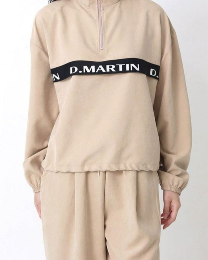 Chamuleのベージュのハーフジップトップス。胸元のロゴラインが特徴で、ゆったりとしたシルエットのスポーティーなゴルフウェア。