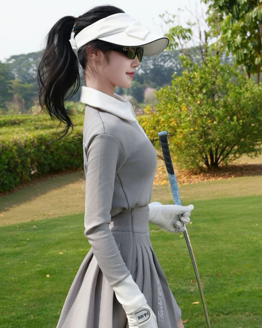 Chamuleのバイカラー長袖ポロとプリーツスカートのゴルフウェアセットアップを着用した女性