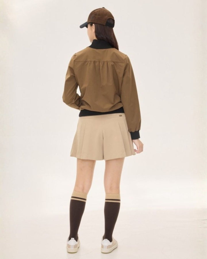Chamuleのバイカラーハーフジップトップスを着用した女性のバックスタイル。ベージュのプリーツスカートと合わせたゴルフウェアコーデ