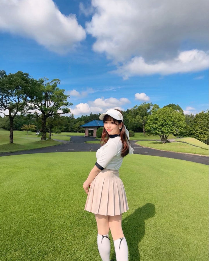 Chamuleのバイカラーリブトップスを着用し、ゴルフ場でポーズをとる女性。襟と袖口がアクセントのスポーティーな半袖ゴルフウェア。