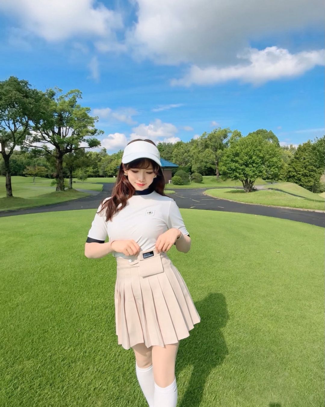 Chamuleのバイカラーリブトップスを着用し、ゴルフ場でポーズをとる女性。白と黒の配色がスポーティーな半袖ゴルフウェア。