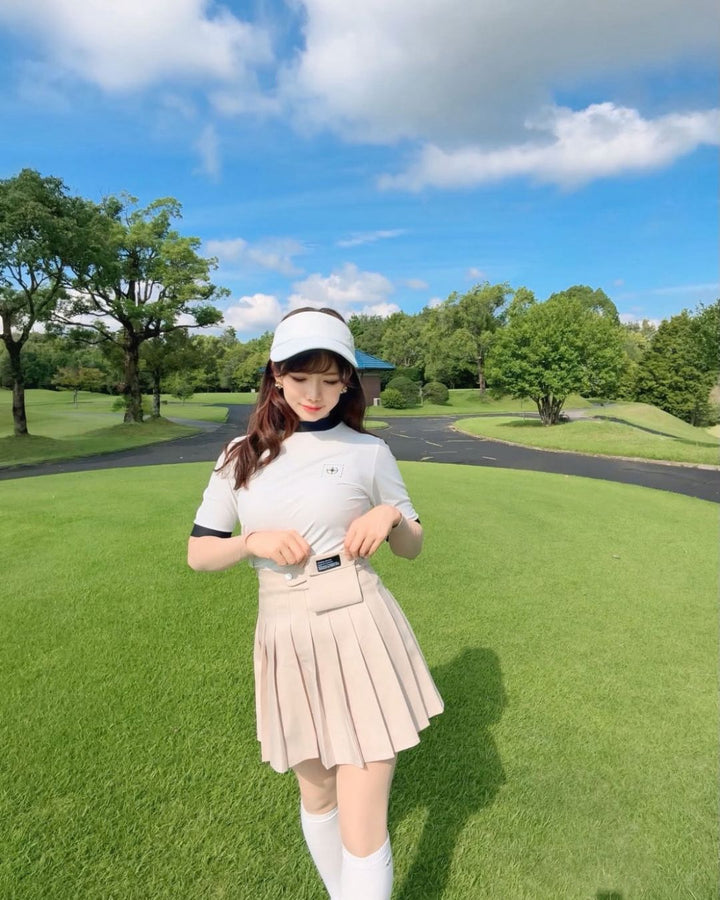 Chamuleのバイカラーリブトップスを着用し、ゴルフ場でポーズをとる女性。白と黒の配色がスポーティーな半袖ゴルフウェア。