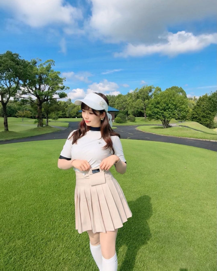 Chamuleのバイカラーリブトップスを着用し、ゴルフ場でポーズをとる女性。襟と袖がアクセントのスポーティーな半袖ゴルフウェア。