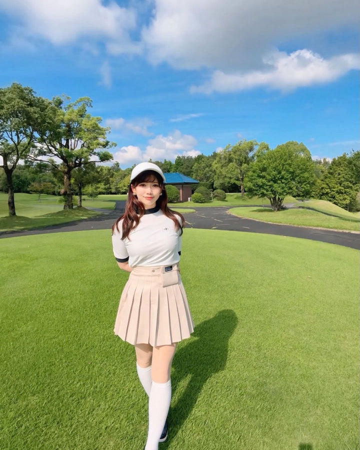 Chamuleのバイカラーリブトップスを着用し、ゴルフ場でポーズをとる女性。襟と袖口がアクセントの半袖ゴルフウェア。