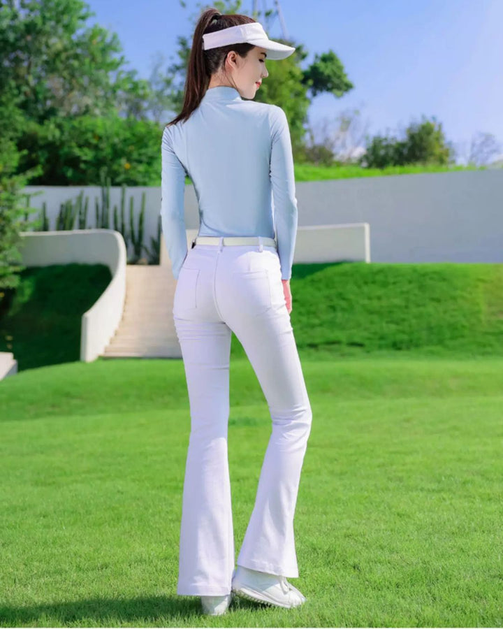 Chamuleの美シルエットフレアゴルフパンツを着用し、ゴルフ場でポーズをとる女性。白のパンツと水色のトップスを合わせたスタイリッシュなゴルフウェア。