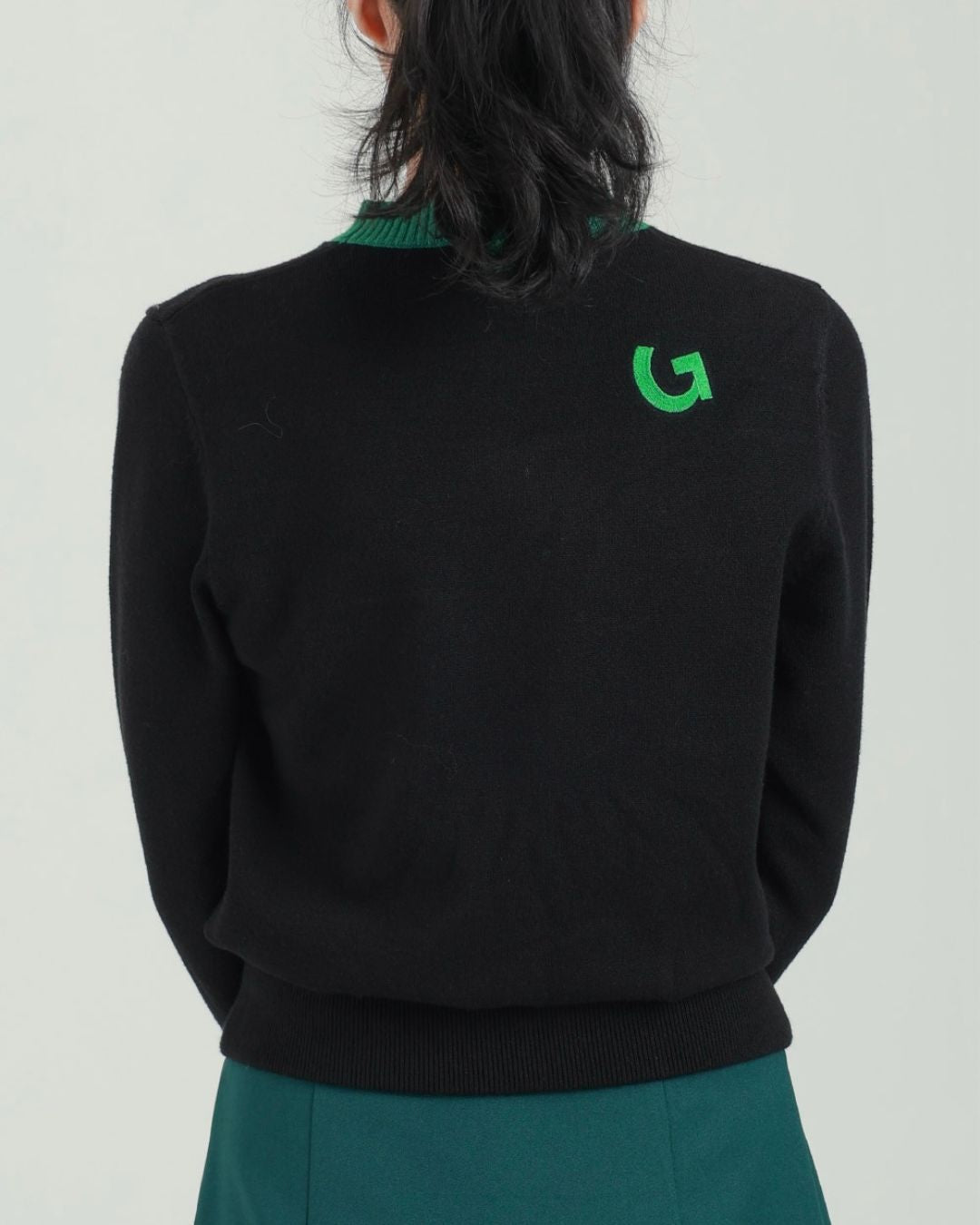 Chamuleのブラックニットトップス。背面にグリーンのロゴ刺繍が施され、襟元もグリーンで統一されたスポーティーなゴルフウェア