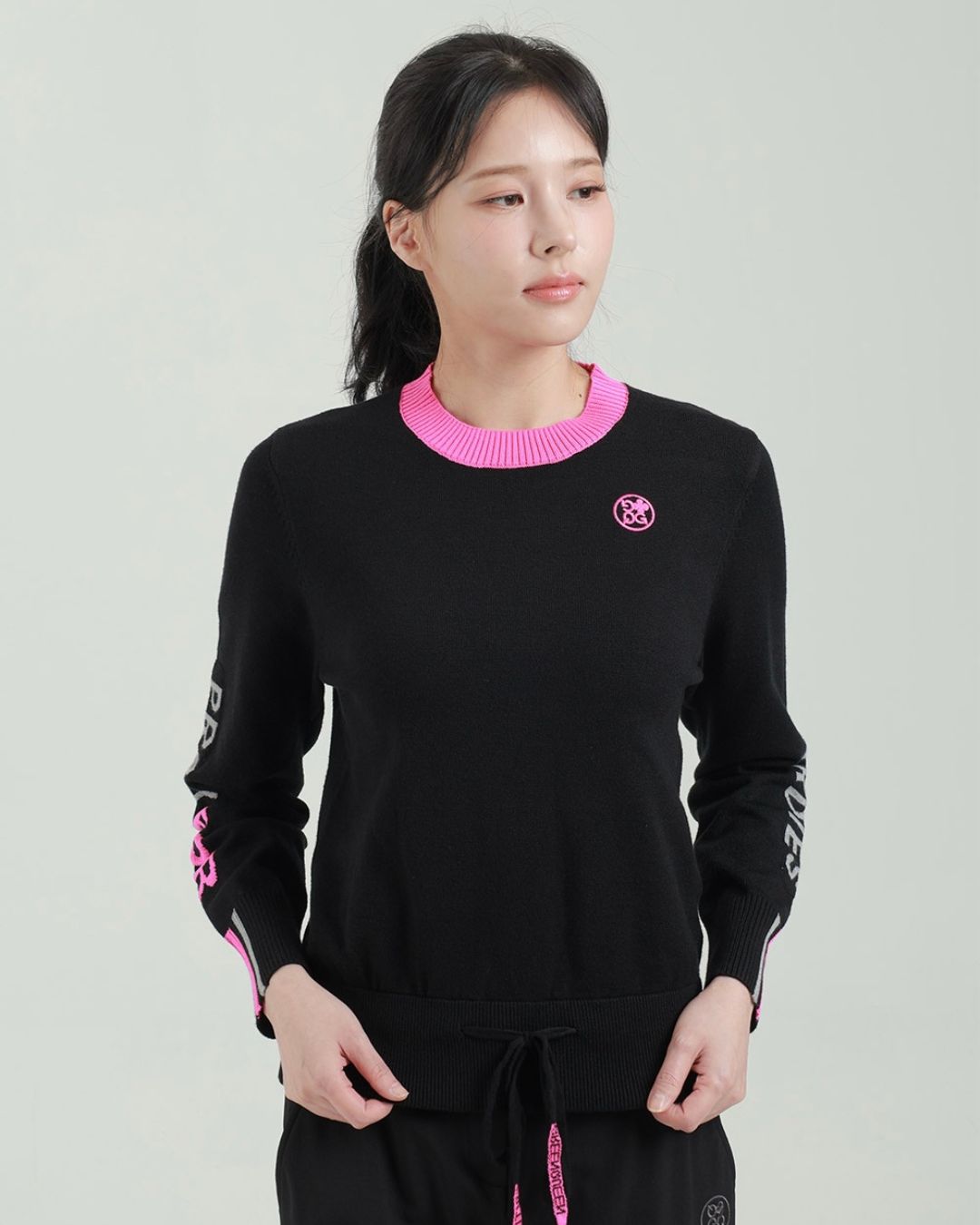 Chamuleのブラックとピンクの配色が鮮やかなスポーティーな長袖ロゴニットトップスを着用した女性モデル