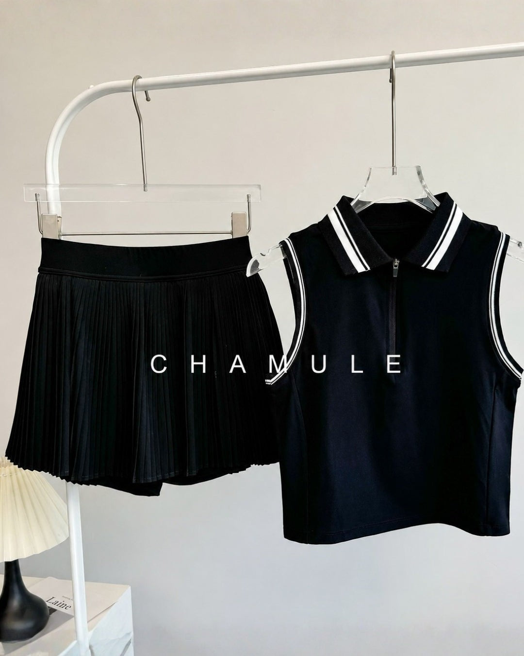 Chamuleの黒いノースリーブトップスとプリーツスカートのセットアップ。襟と袖のラインが特徴的なゴルフやテニスに最適なウェア。