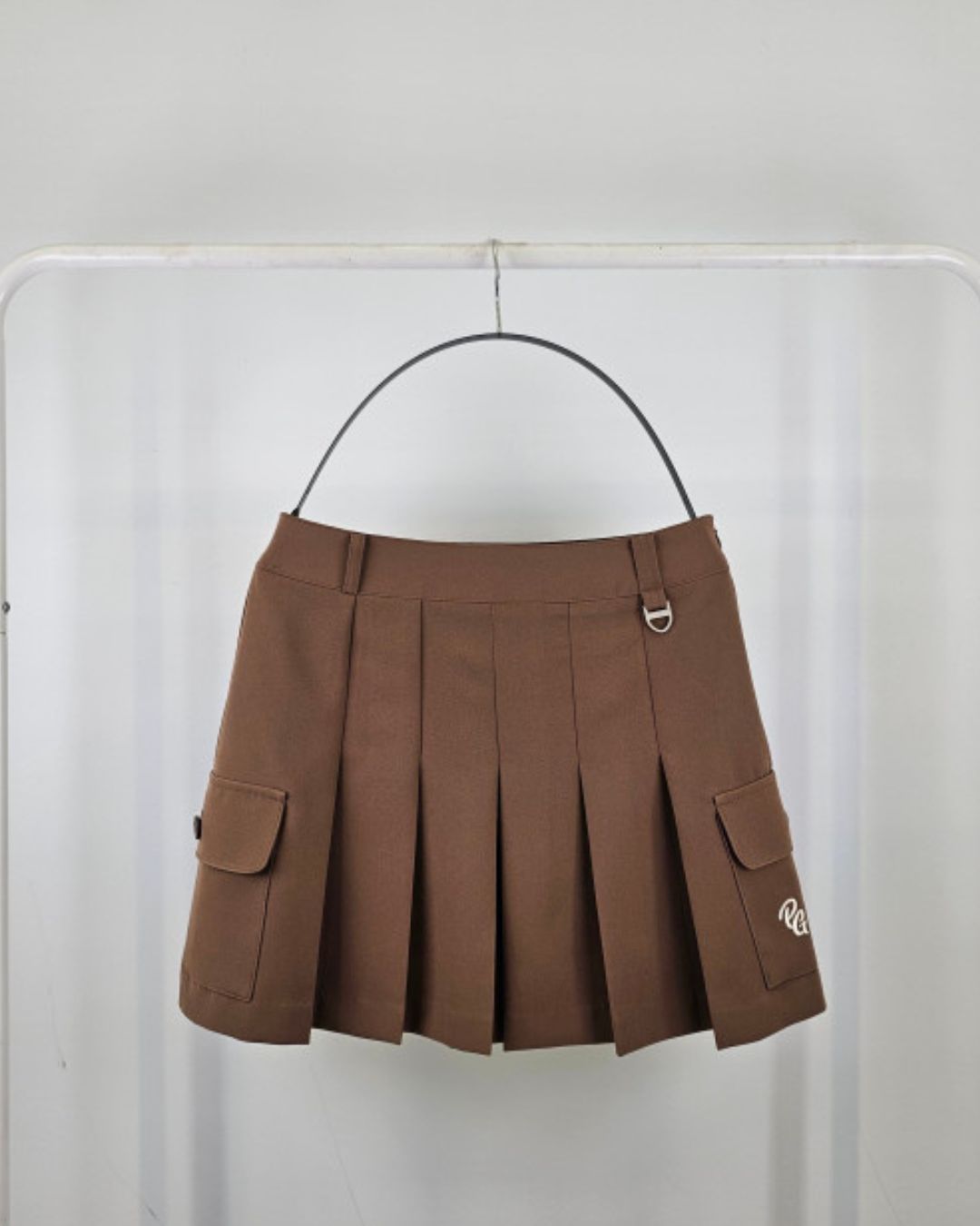 Chamuleのブラウンのカーゴポケット付きプリーツスカート。サイドにフラップポケットとロゴ刺繍、ウエストにDカンを備えたゴルフウェア