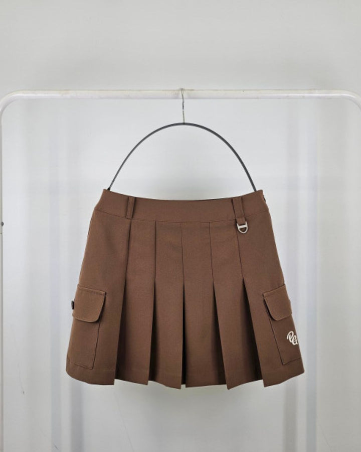 Chamuleのブラウンのカーゴポケット付きプリーツスカート。サイドにフラップポケットとロゴ刺繍、ウエストにDカンを備えたゴルフウェア