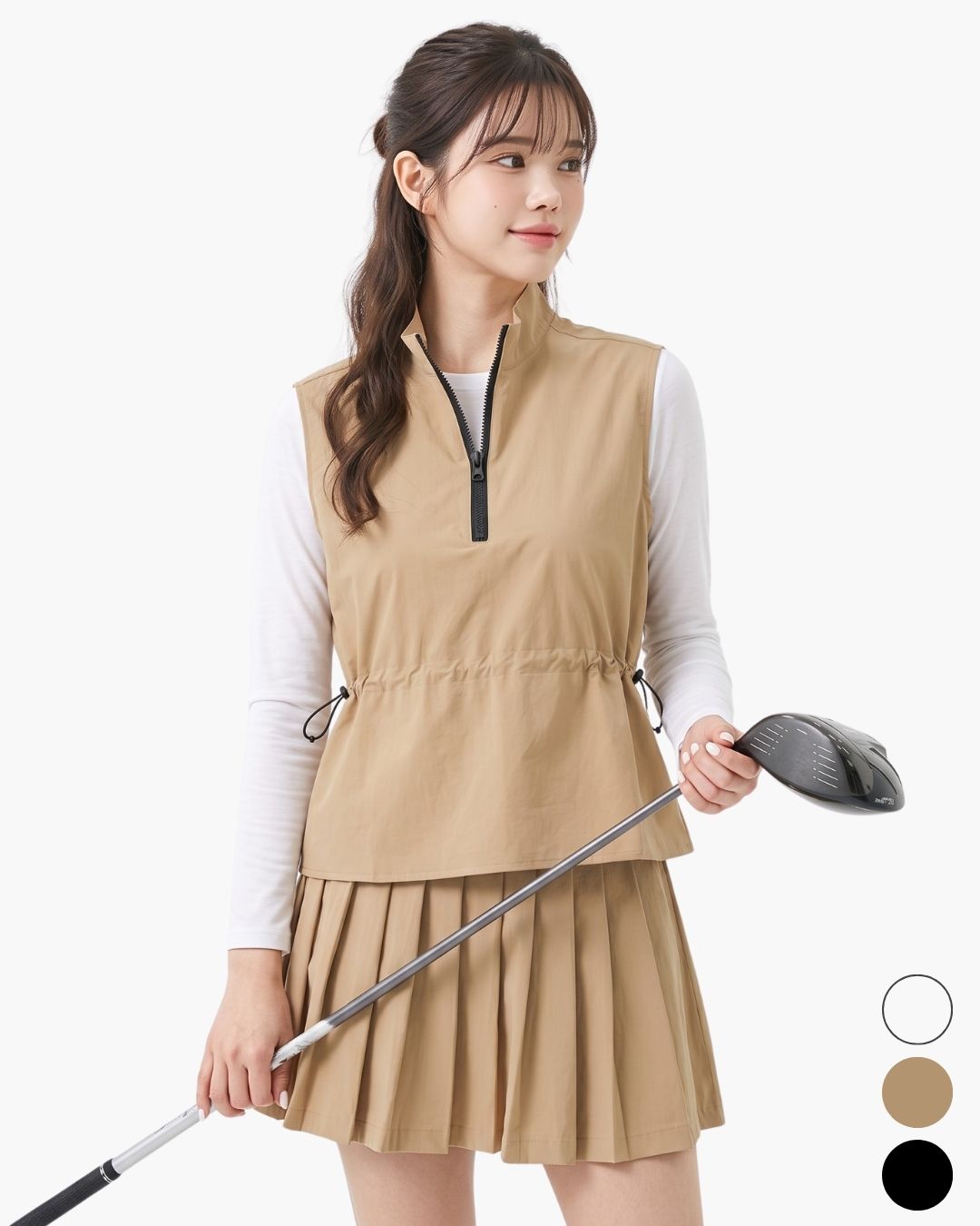 Chamuleのベージュのハーフジップベストとプリーツスカートのセットアップを着用した女性ゴルファー