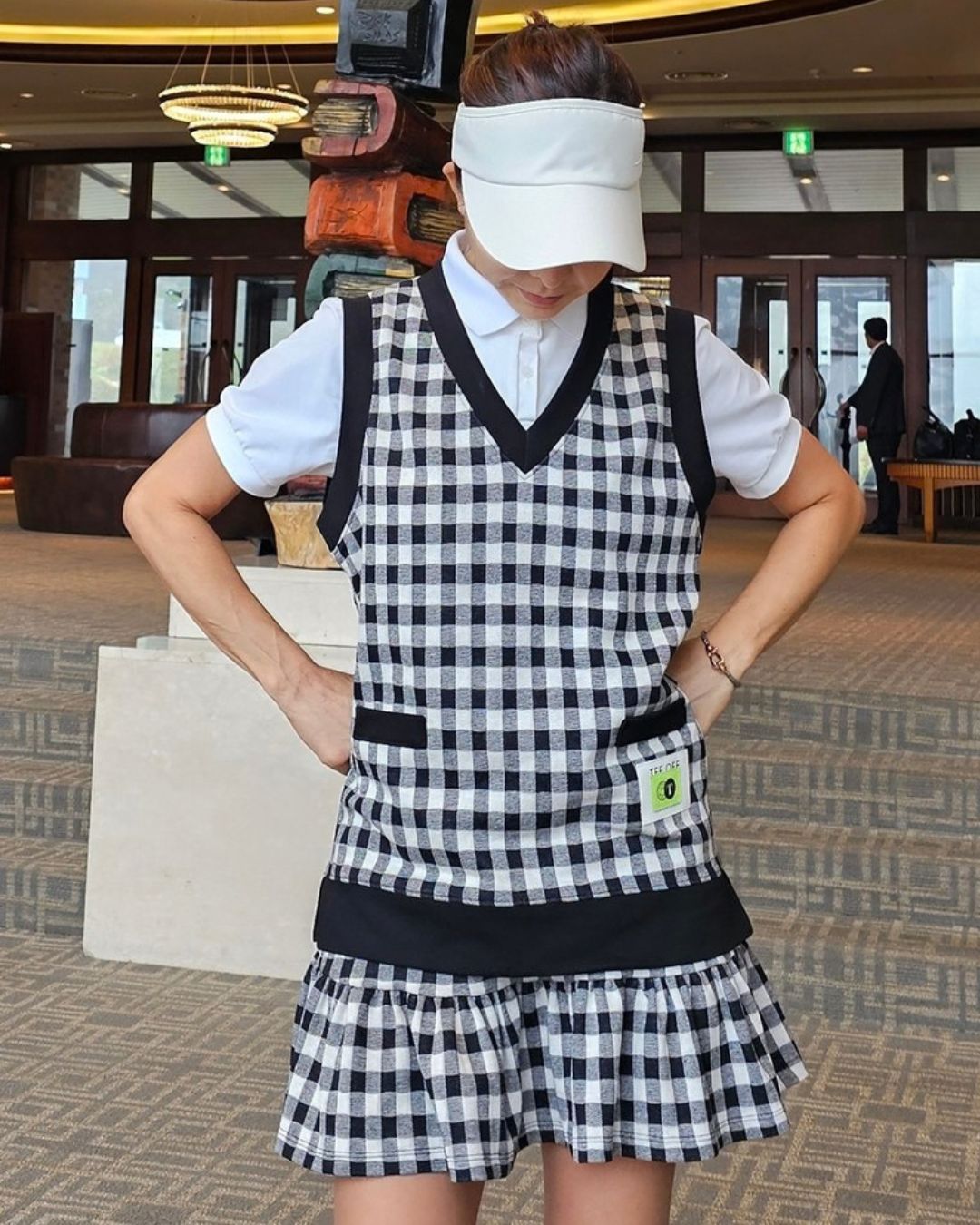 Chamuleのギンガムチェック柄Vネックベストを着用したゴルフウェアスタイル。黒と白の配色でポケットがアクセント。