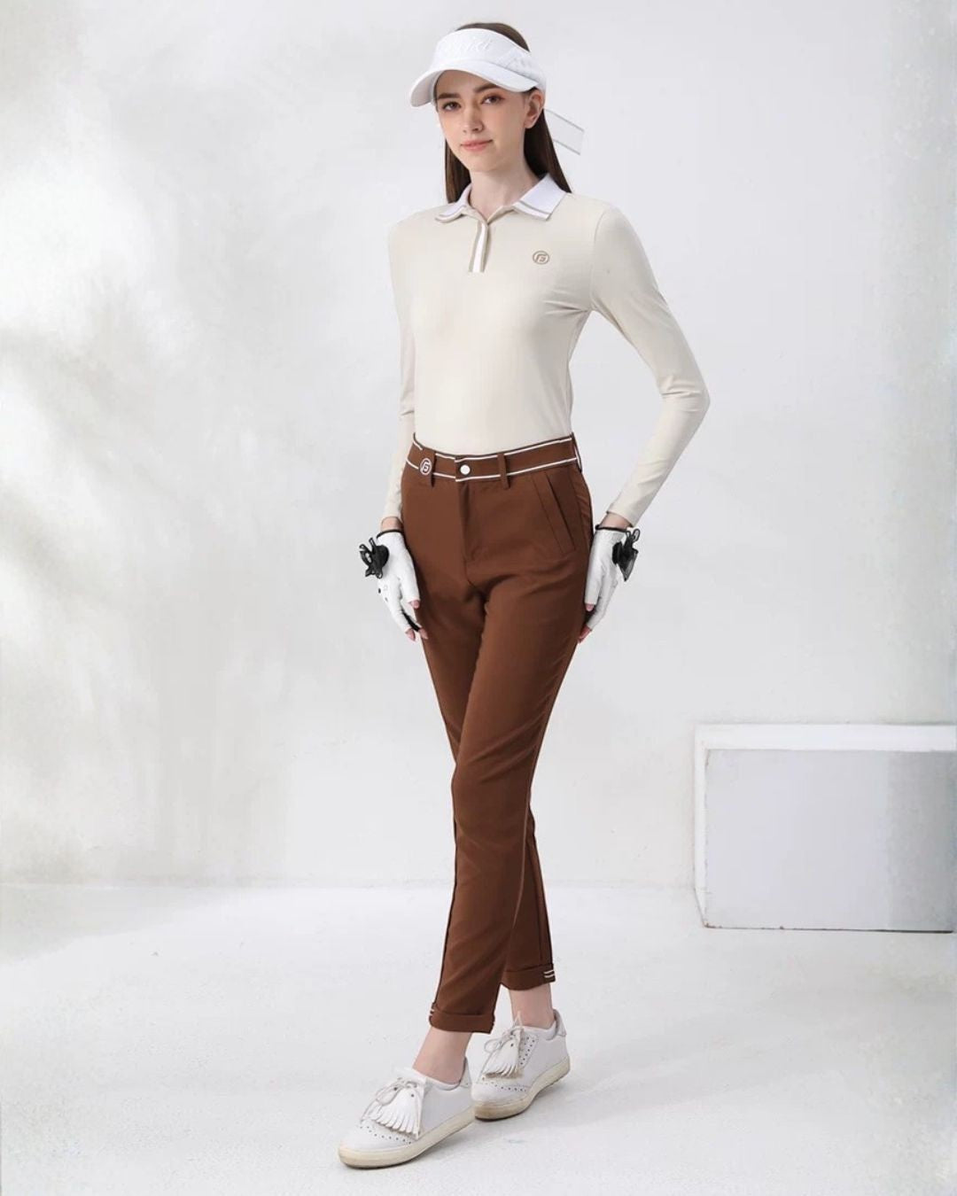 Chamuleのアイボリーの長袖ポロシャツとブラウンのパンツを着用した女性ゴルファーの全身コーディネート