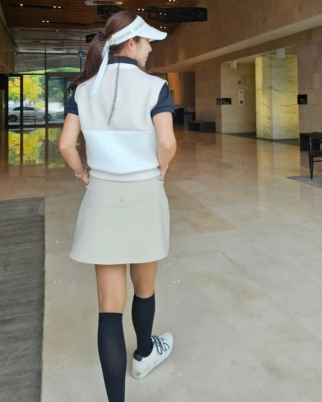 Chamuleのベージュとホワイトのミニマルなゴルフベストを着用した女性のバックスタイル