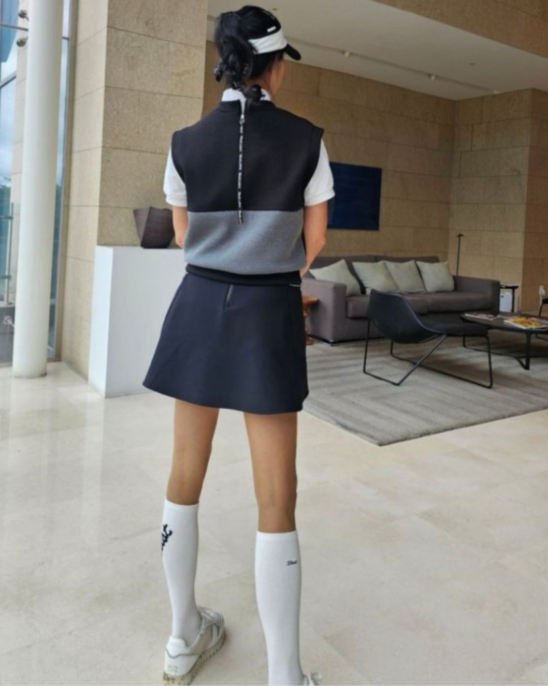 Chamuleのシンプルゴルフベストを着用した女性。黒とグレーのバイカラーデザインで、背面にジッパーが施された上品なゴルフウェア。