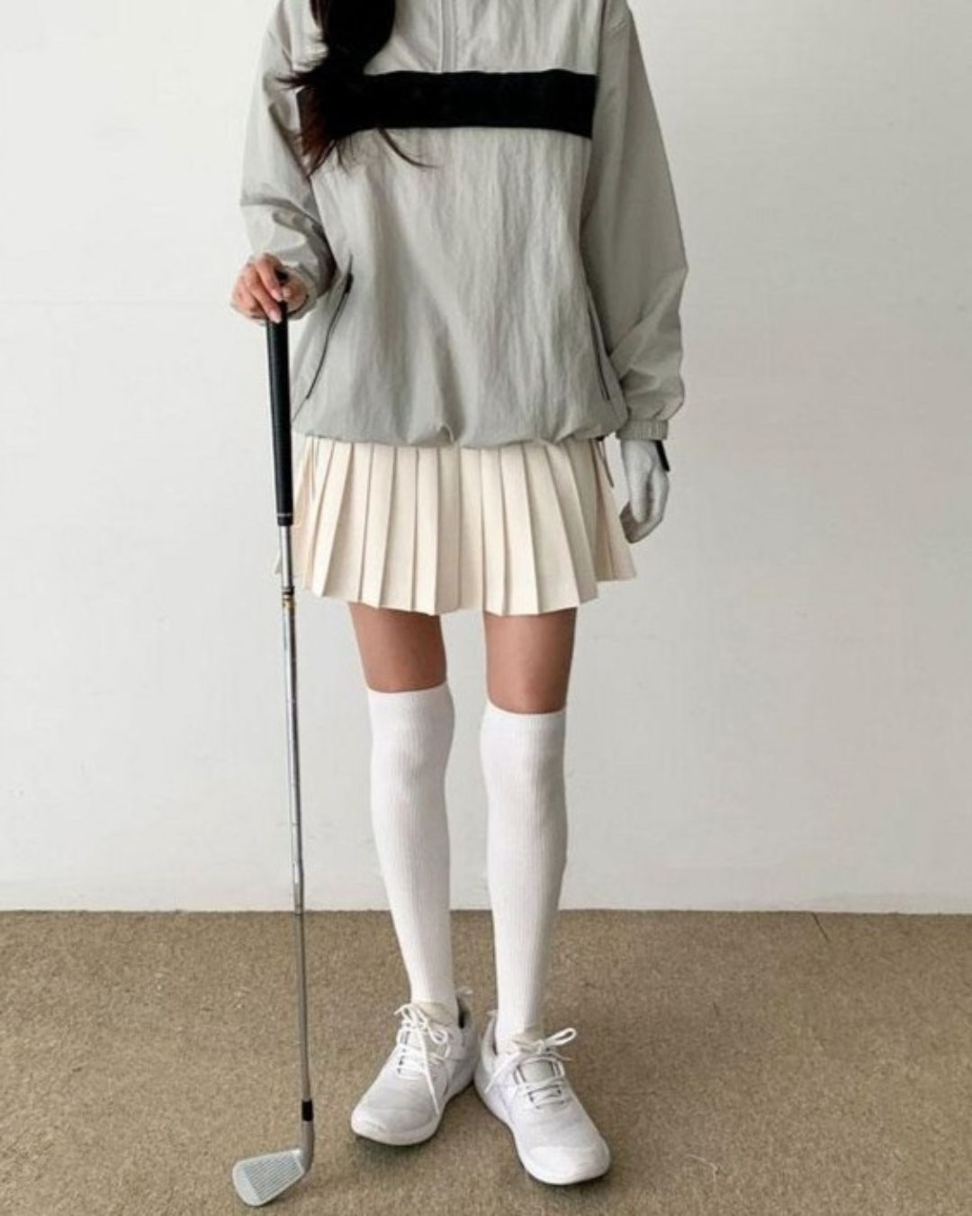 Chamuleの胸元に黒いラインが入ったグレーのハーフジップトップスとベージュのプリーツスカートを合わせたゴルフウェア