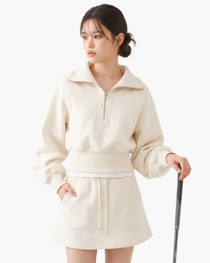 Chamuleのハーフジップフーディとミニスカートのセットアップ。柔らかなアイボリーカラーのスポーティーで女性らしいゴルフウェア。