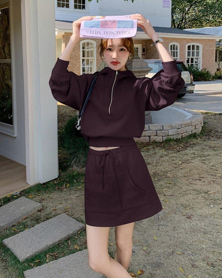Chamuleのダークブラウンのハーフジップスウェットトップスとミニスカートのセットアップを着用した女性