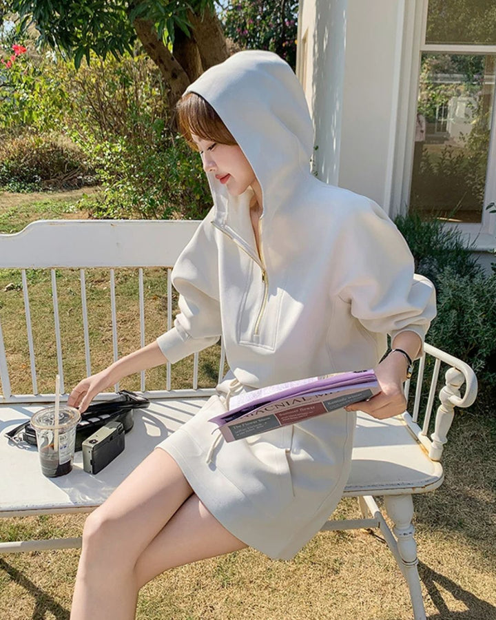 Chamuleのオフホワイトのハーフジップパーカーとミニスカートのスポーティーなセットアップを着た女性がベンチに座っている様子