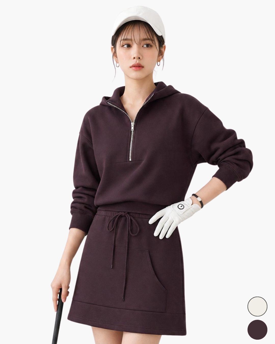 Chamuleのダークブラウンのハーフジップスウェットとミニスカートのセットアップを着用した女性ゴルファー