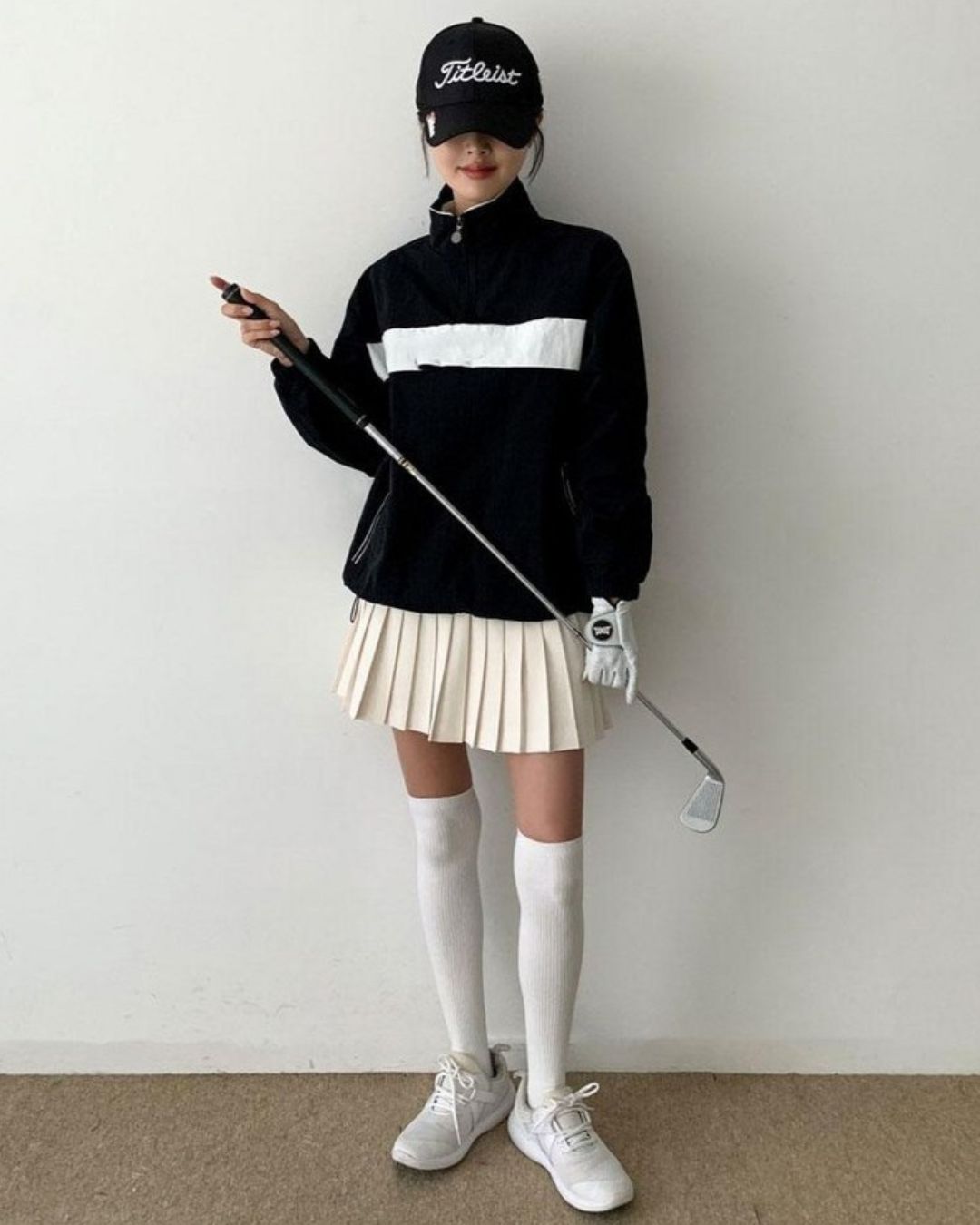 Chamuleの胸元に白いラインが入った黒いハーフジップトップスを着用し、ゴルフウェアでコーディネートした女性