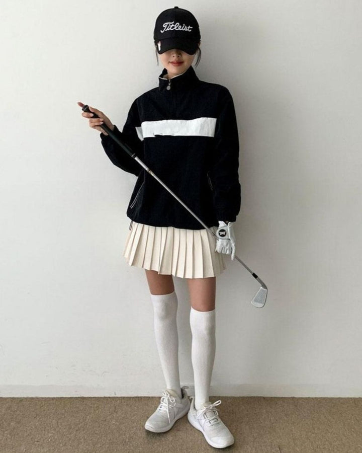 Chamuleの胸元に白いラインが入った黒いハーフジップトップスを着用し、ゴルフウェアでコーディネートした女性