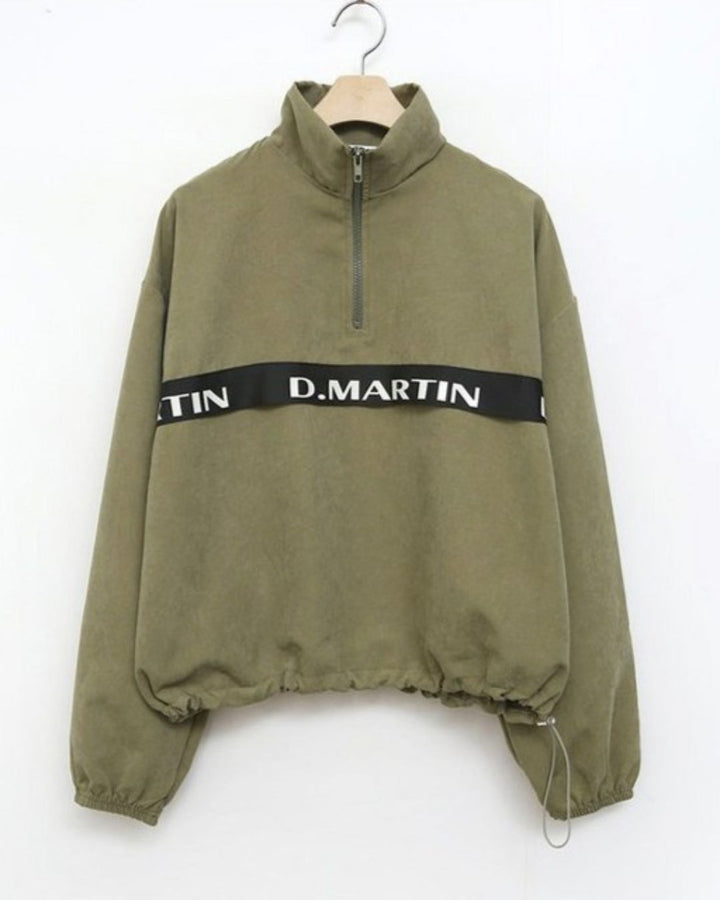 Chamuleのロゴライン入りカーキ色ハーフジップトップス。ゆったりとしたシルエットで裾にドローコード付き。