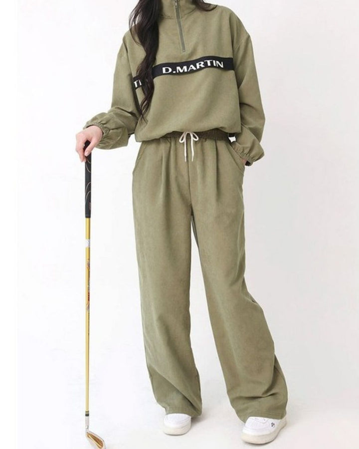 Chamuleのロゴライン入りカーキ色ハーフジップトップス。ゆったりとしたシルエットで裾にドローコード付きのスポーティーなゴルフウェア。