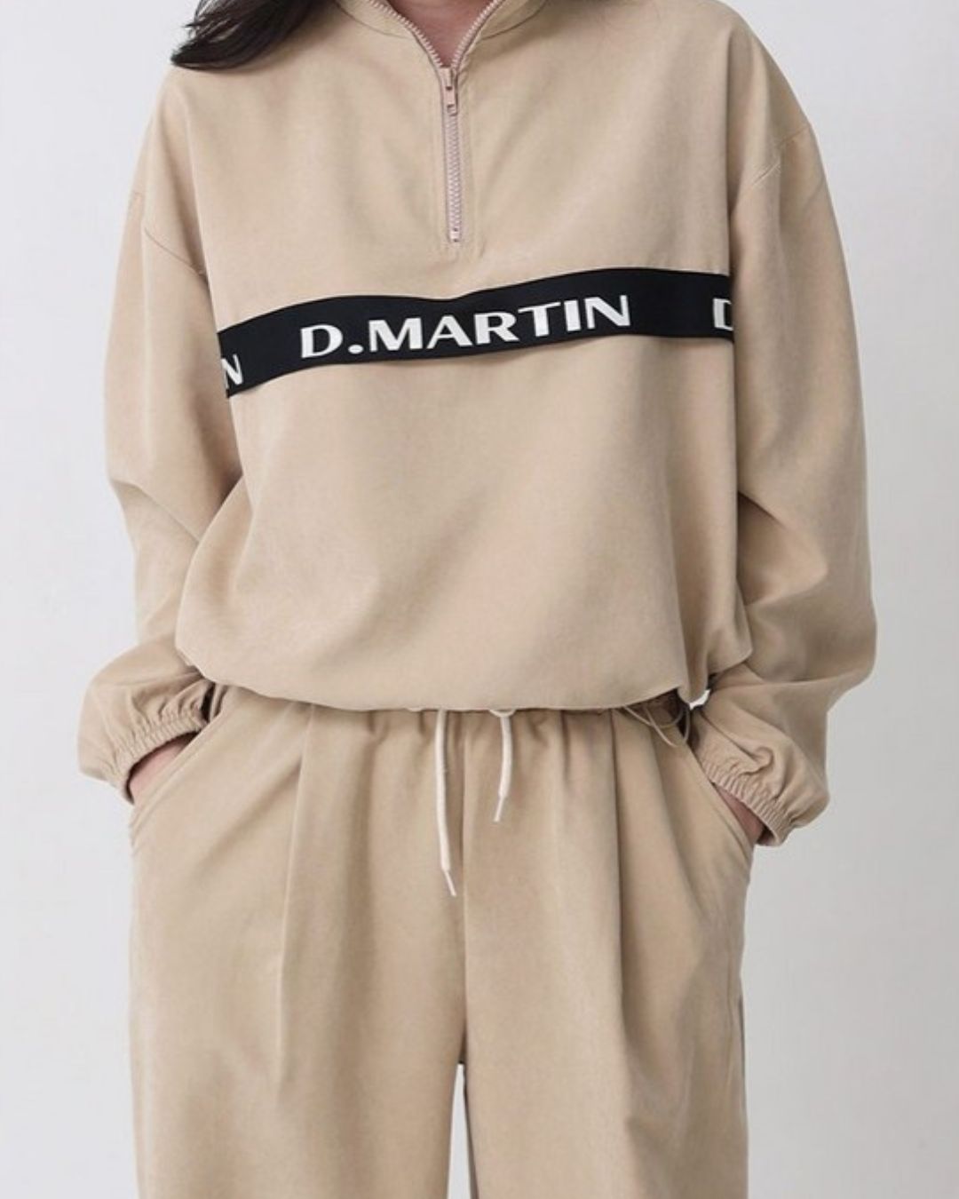 Chamuleのベージュのハーフジップトップス。胸元のロゴラインが特徴で、ゆったりとしたシルエットのスポーティーなゴルフウェア。