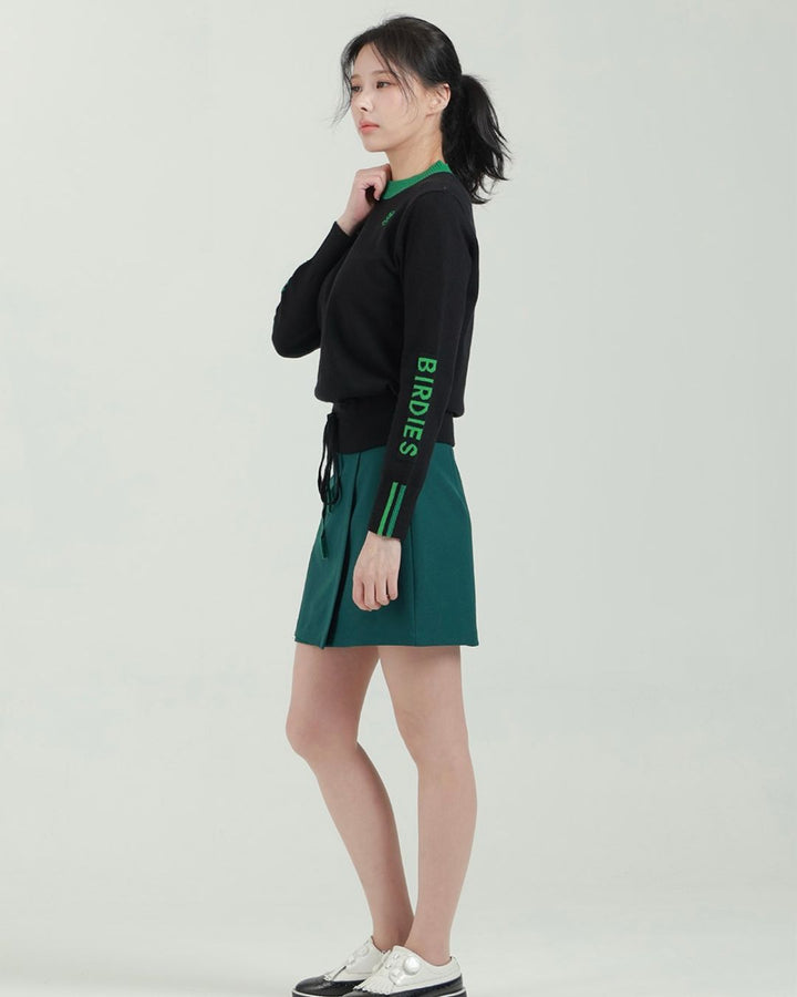 Chamuleのブラックとグリーンのロゴ入り長袖ニットトップスを着用した女性モデルのサイドビュー
