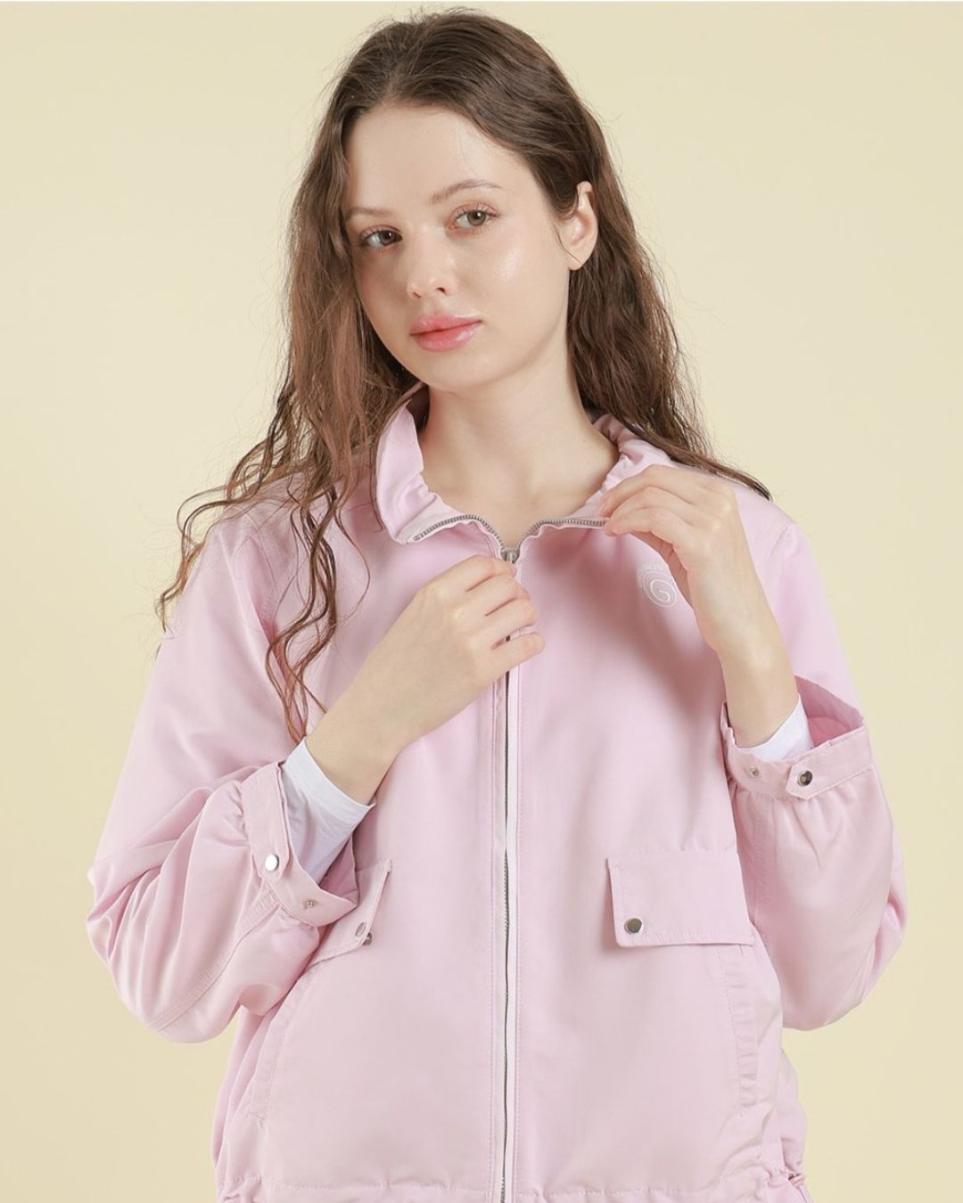 Chamuleの淡いピンク色の軽量フーディブルゾンを着用した女性。フロントジップとポケットが特徴のゴルフウェア。