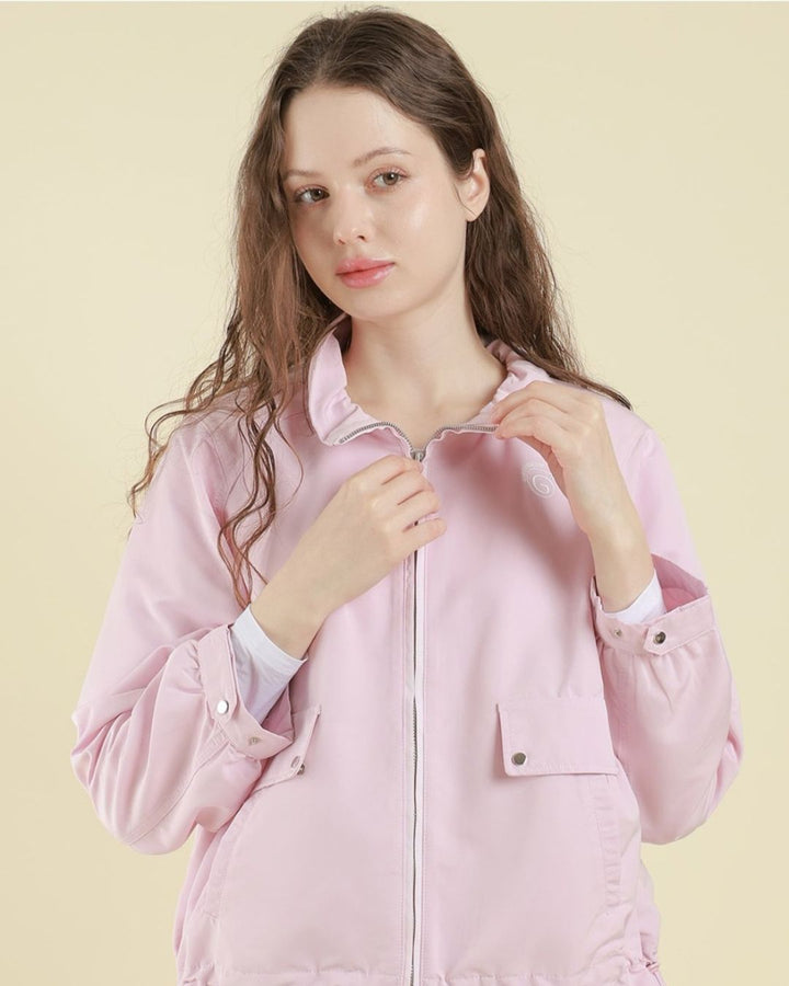 Chamuleの淡いピンク色の軽量フーディブルゾンを着用した女性。フロントジップとポケットが特徴のゴルフウェア。
