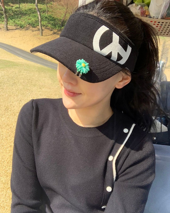 Chamuleのロゴ入り黒色コットン製ゴルフサンバイザーを着用した女性。花形のクリップがアクセントのスポーティーなデザイン。
