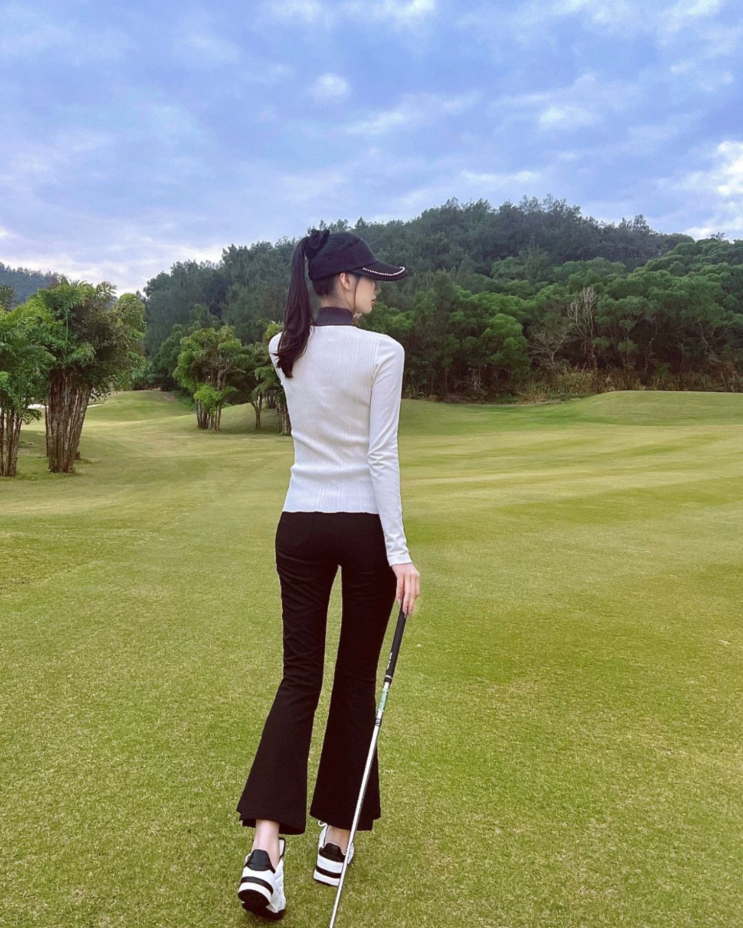 Chamuleの裏起毛スリムフレアゴルフパンツを着用し、ゴルフ場でポーズをとる女性の後ろ姿