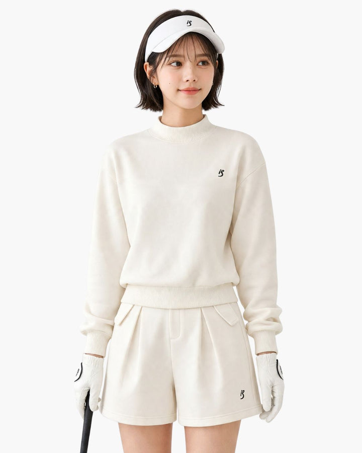 Chamuleのワンポイントロゴ入りホワイトゴルフウェアセットアップ。トップスとショートパンツを着用した女性ゴルファー